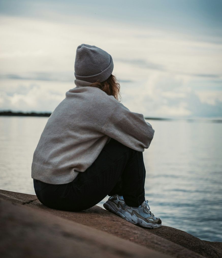 Femme assise face à la mer, perdue dans ses pensées : accompagnement de la dépression par le ressenti à Lyon