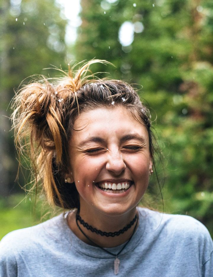 Femme riant les yeux fermés dans la nature : apprendre à s'écouter et se reconnecter à son ressenti